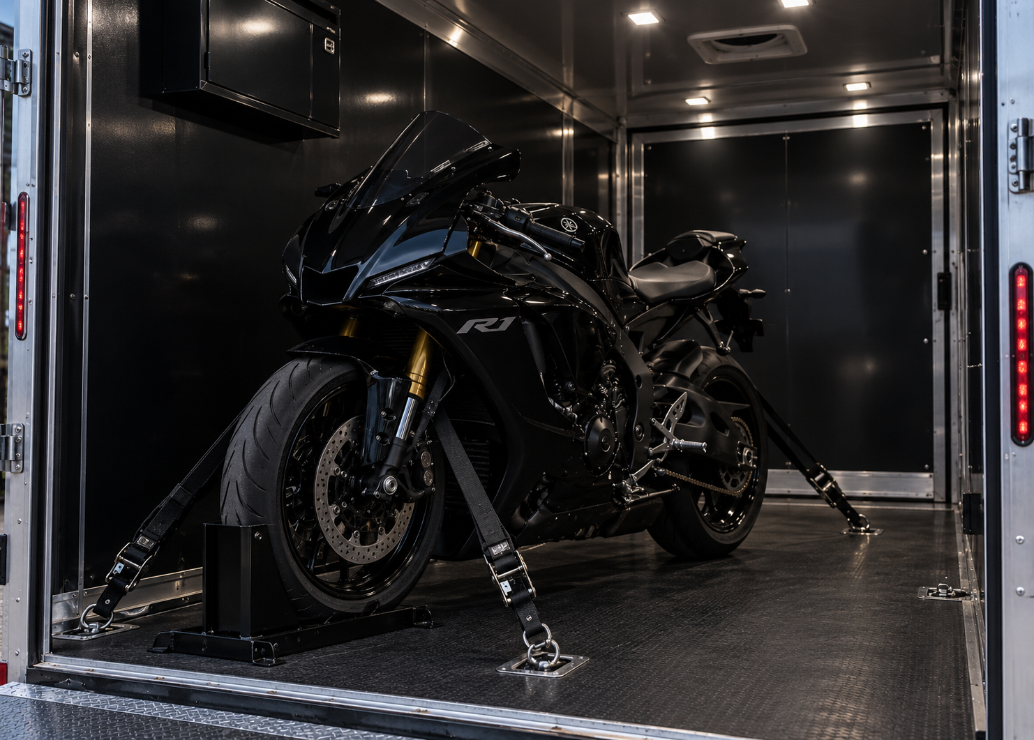 Black Yamaha R1 sportbike strapped down inside a lit enclosed motorcycle trailer